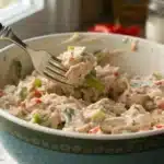 Creamy tuna salad being mixed with a fork in a bowl, showing fresh texture